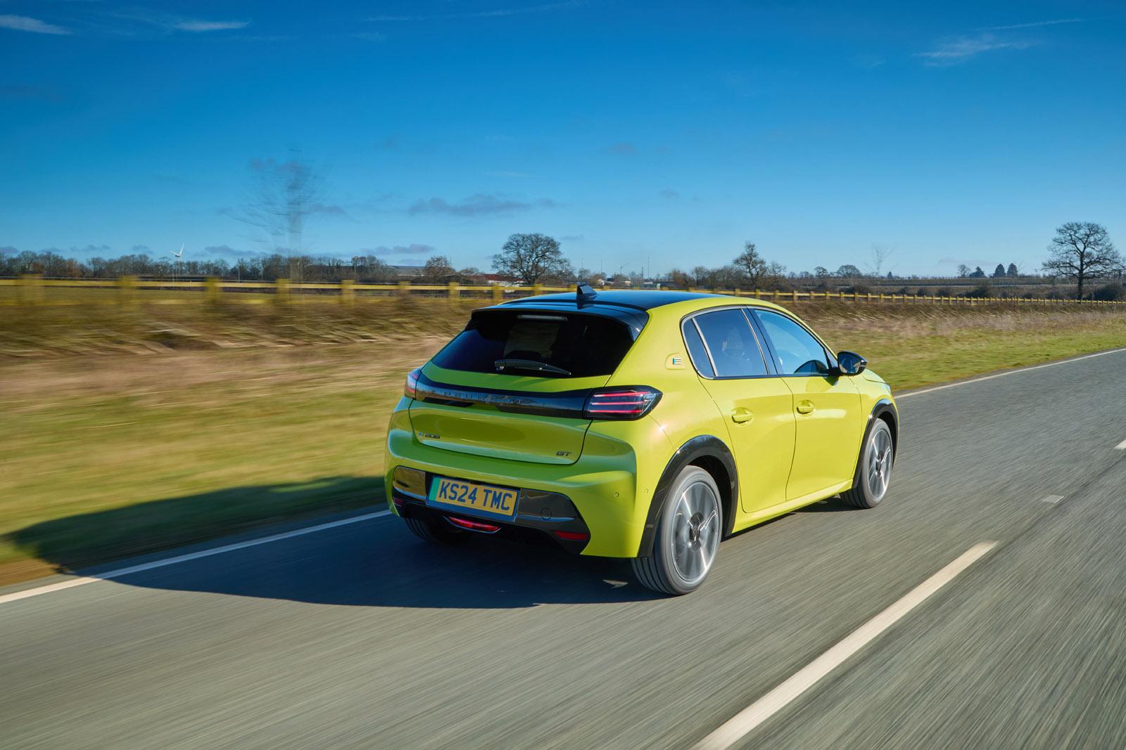 Bright yellow hatchback car driving on a rural road with clear blue sky and fields in the background.