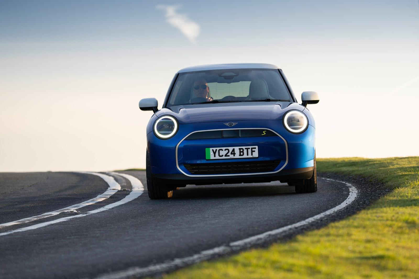 A blue car with round headlights drives on a winding road, with a clear sky in the background. License plate reads "YC24 BTF."
