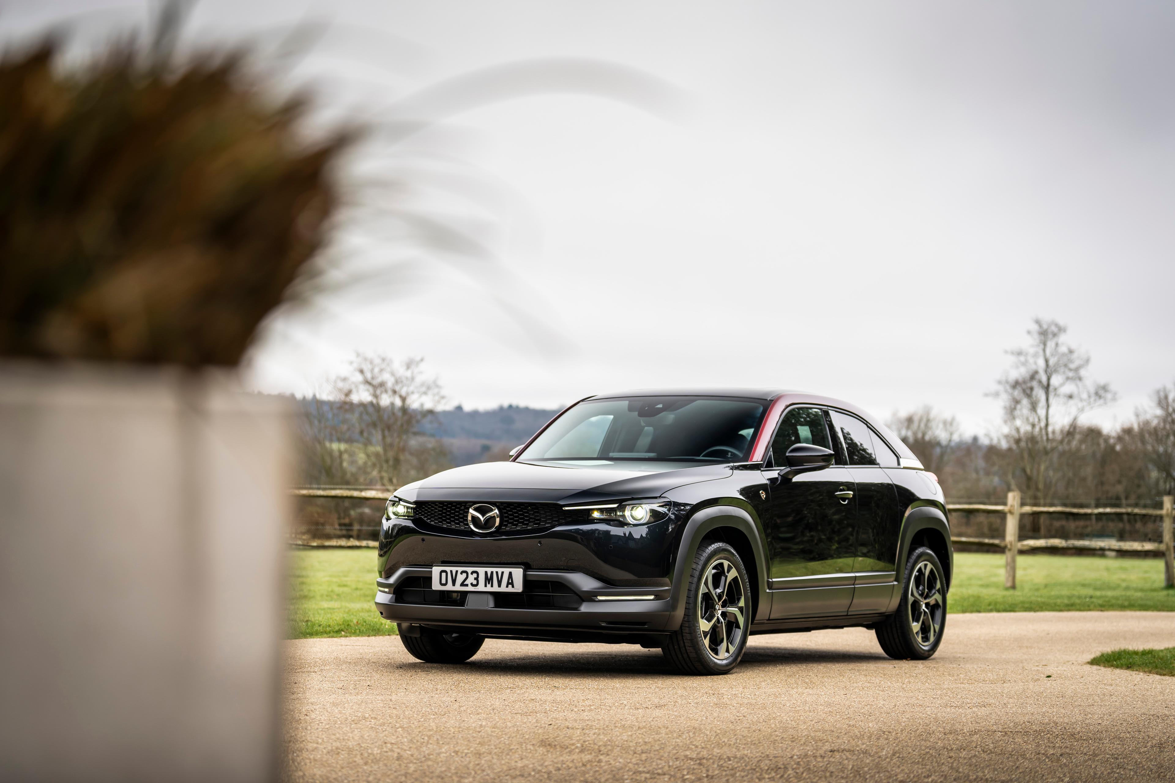 A sleek black Mazda SUV parked on a driveway with a grassy field and wooden fence in the background.