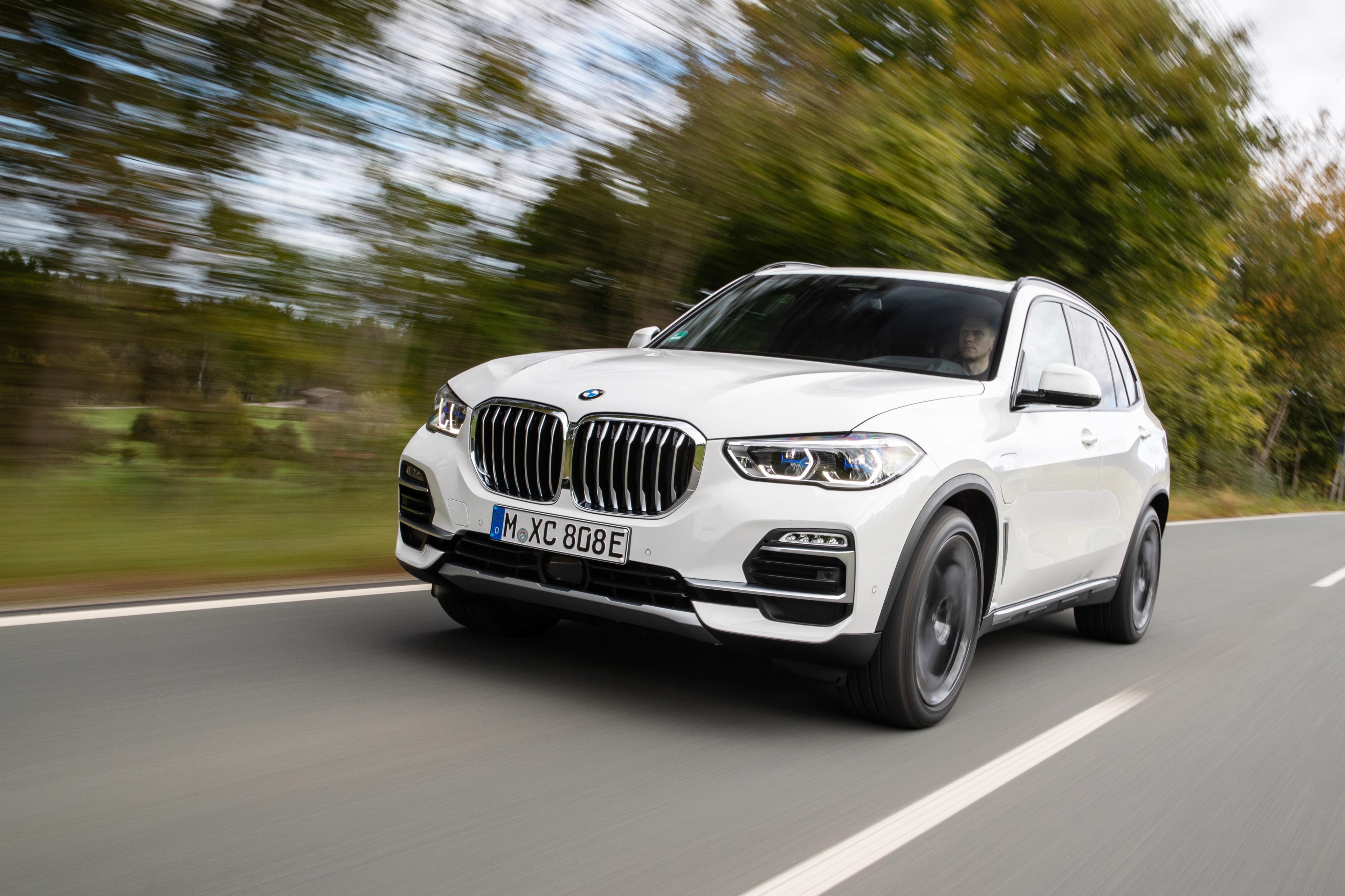 a white BMW X5 xDrive45e driving on a road next to trees