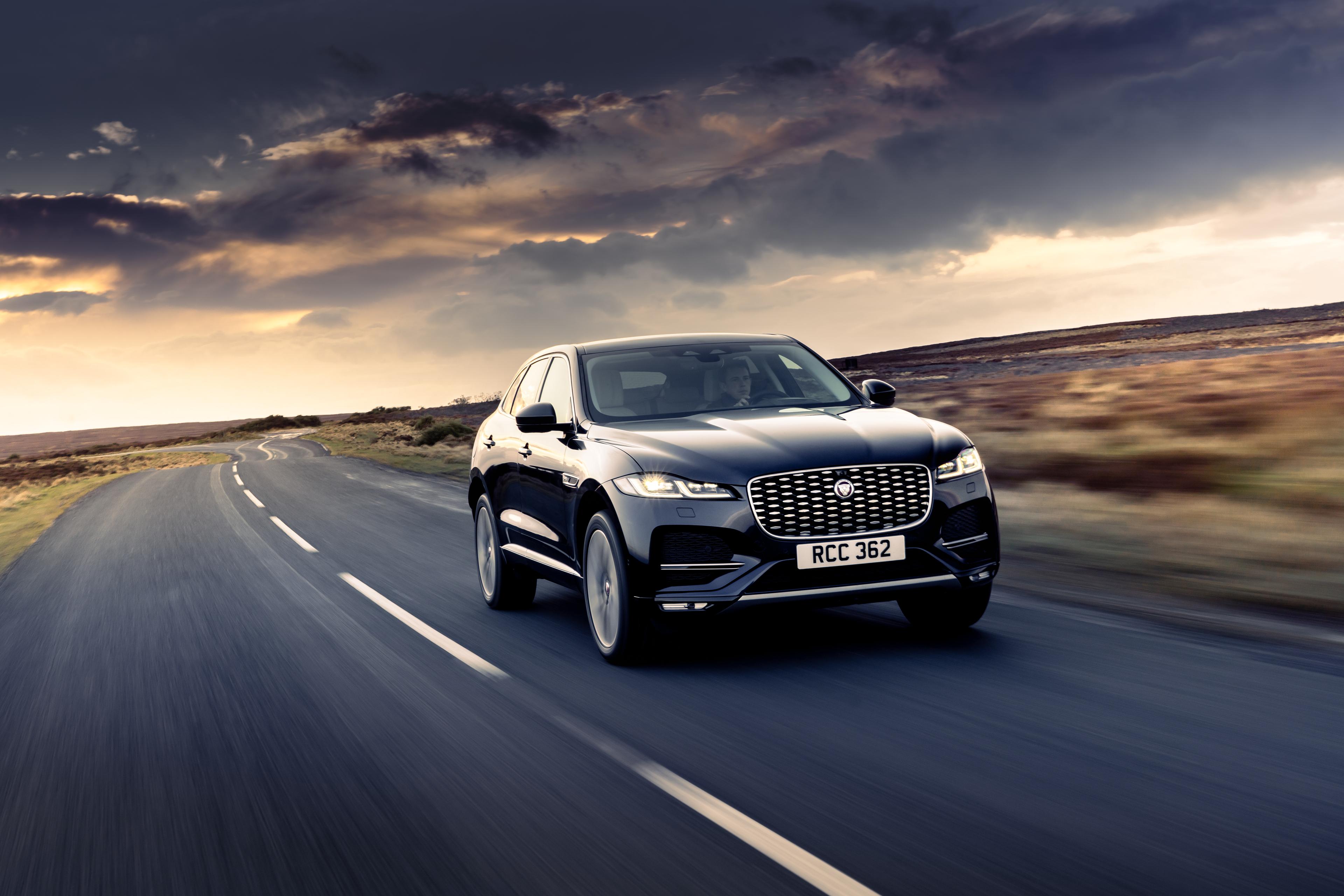 a black Jaguar F-Pace P400e driving along a countryside road at sunset